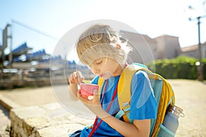 Happy little boy eating tasty ice cream in paper cup outdoors. School child have ice-cream snack on the go after school on sunny