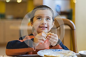 Happy little boy eats pancakes hands. Portrait of small cute little boy child caucasian sitting by the table at home eating