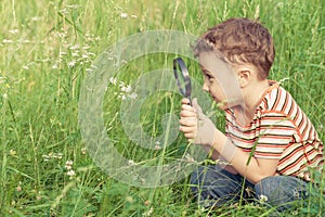 Happy little boy exploring nature with magnifying glass