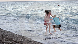 Happy little boy and girl having fun and jumping on the beach in the evening.