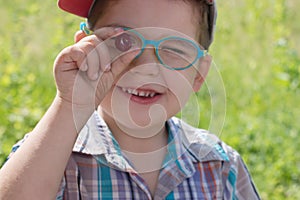 Happy little boy in glasses holds cherry at summer day outd