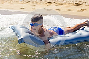 Happy little boy in goggles lying on air water mattress in sea