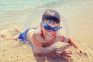 Happy little boy in googles toothy smile on beach in water