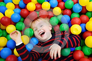 Happy little boy having fun in ball pit with colorful balls