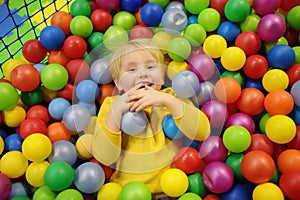 Happy little boy having fun in ball pit with colorful balls. Child playing on indoor playground