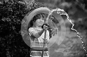 Happy little boy having fun in domestic garden. Child hold watering garden hose. Active outdoors games for kids in the