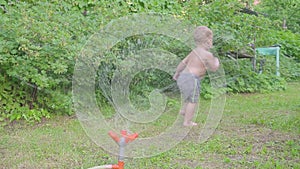 Happy little boy having fun outside with water sprinkler in summer garden. Slow motion