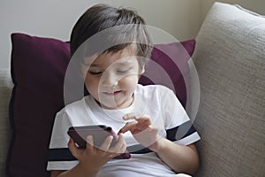 Happy little boy having fun playing game on mobile phone,Preschool kid sititng on sofa with smiling face watching cartoon on smart