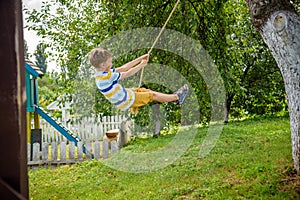 Happy little boy is having fun on a rope swing which he has found while having rest outside city. Active leisure time with