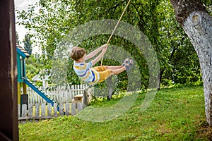 Happy little boy is having fun on a rope swing which he has found while having rest outside city. Active leisure time with