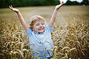 Happy little boy having fun in wheat field in summer