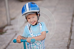 Happy little boy with helmet, playing with his scooter outdoor