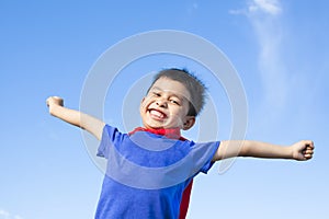 Happy little boy imitate superhero and open arms with blue sky