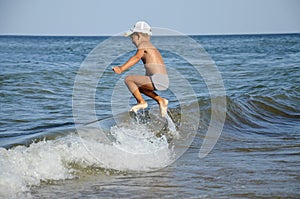 A happy little boy jumps over a sea wave