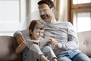 Happy little boy laughing at story, reading book with father.