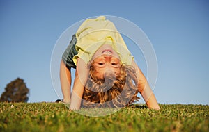 Happy little boy laying upside down on grass. Kids exploring nature, summertime.