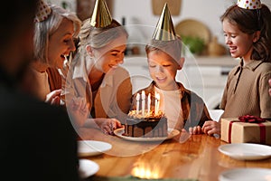 Happy little boy making wish and going to blow candles on cake while celebrating Birthday with big family