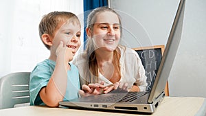 Happy little boy with mother smiling and looking on laptop screen. Amazed child using laptop computer