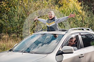 happy little boy with open arms standing in open car sunroof while father driving car