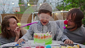 Happy little boy with parents blowing birthday candles. Parents dip a child face in a cake.