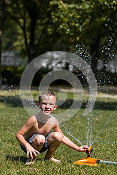 Happy little boy play in water drops from irrigation gardening hose