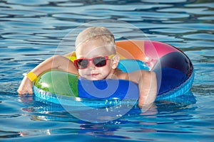 Happy little boy playing with colorful inflatable ring in outdoor swimming pool on hot summer day. Kids learn to swim. Child water