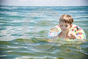 Happy little boy playing with colorful inflatable ring in outdoor swimming sear river lake or pool on hot summer day. Kids learn