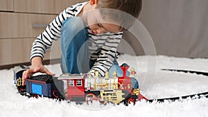 Happy little boy playing on the floor in the room. A child with a toy railway. Home classes for children. Children's