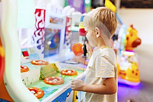 Happy little boy playing fun games on arcade machine at an amusement park