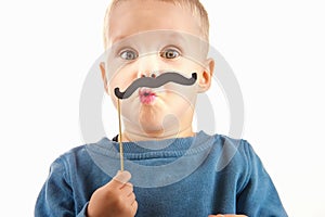 Happy little boy playing with a paper mustache, laughing while d