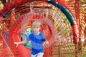 Happy little boy playing in rope tunnel at the modern playground. Summer holidays. Happy and healthy childhood