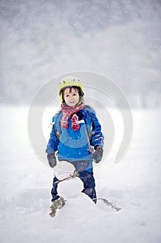 Happy little boy playing in the snow while snowing, helmet
