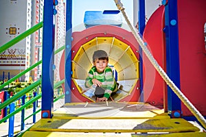 Happy little boy playing in tube or tunnel at the modern playground. Summer holidays. Happy and healthy childhood