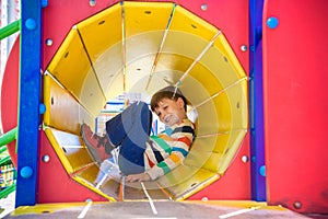 Happy little boy playing in tube or tunnel at the modern playground. Summer holidays. Happy and healthy childhood