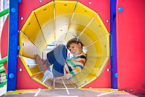 Happy little boy playing in tube or tunnel at the modern playground. Summer holidays. Happy and healthy childhood