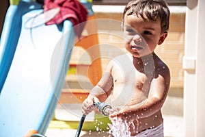 Happy little boy playing with water hose in the backyard