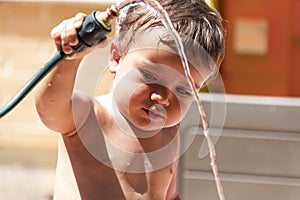 Happy little boy playing with water hose in the backyard