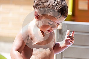 Happy little boy playing with water hose in the backyard