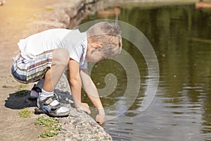 Happy little boy playing with water at the pond in the city park