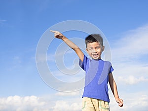 Happy little boy pointing direction with blue sky