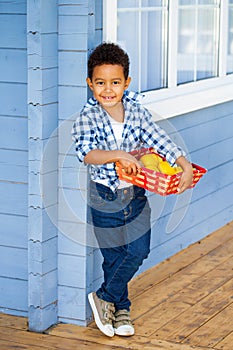 Happy little boy on the porch of the house with fruits