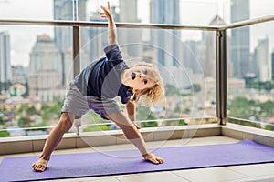 Happy little boy is practicing yoga on his balcony with a panoramic view of the big city