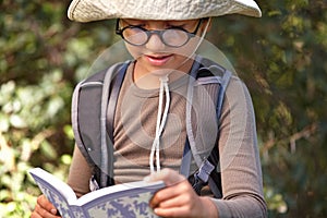 Happy, little boy and reading book in forest for travel guide, adventure or outdoor discovery. Male person, child or kid