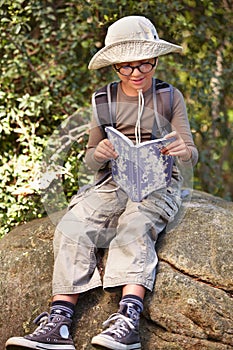 Happy, little boy and reading in nature with book for travel guide, adventure or outdoor discovery. Male person, child