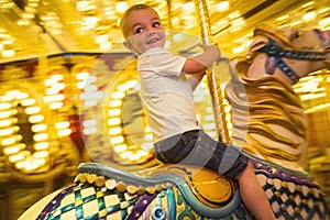 Happy little boy riding a merry go round carousel with bright lights