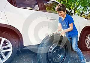 Happy little boy rolling donut tire next to a car