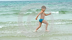 Happy little boy running along the sea shore at tropical beach