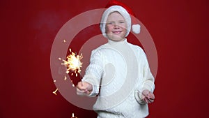 Happy little boy in Santa Claus cap holding bengal light on the red background