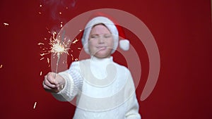 Happy little boy in Santa Claus cap holding bengal light on the red background