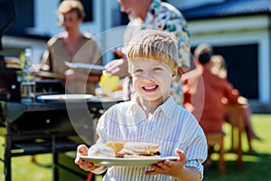 Happy little boy serving burgers at multi generation garden party in summer.